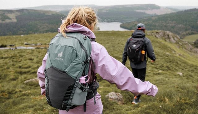 Hikers with backpacks walking through grassy hills overlooking a lake